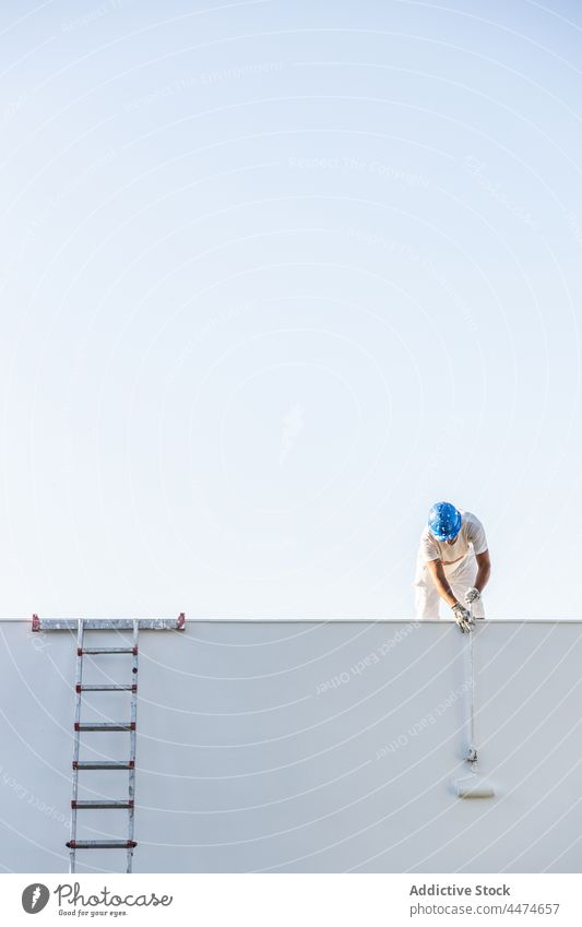 Front view of a young painter painting from the roof man helmet occupation individuality safety splattered stained sky working copy space ladder dirty