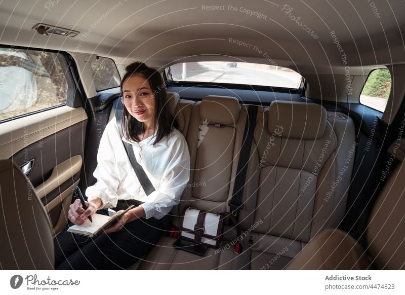 Smile ethnic woman taking notes in notebook in taxi enjoy passenger backseat ride cab write comfort female commute busy service transport read optimist