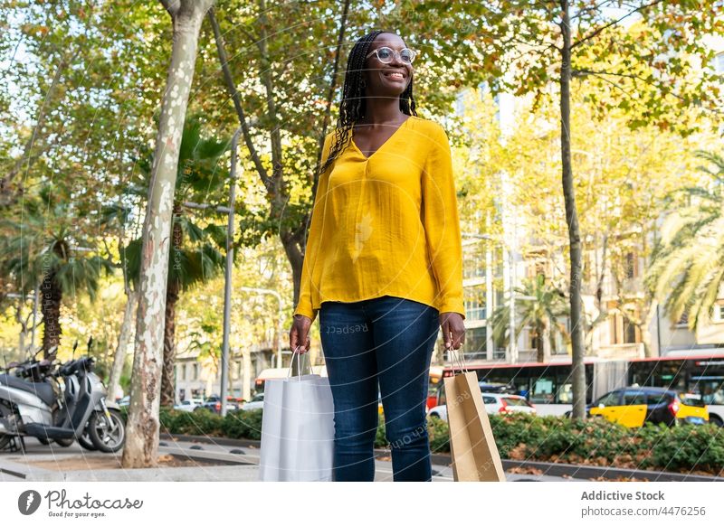 Cheerful black woman with shopping bags on street shopper purchase customer consume shopaholic sidewalk city african american female road lady positive cheerful