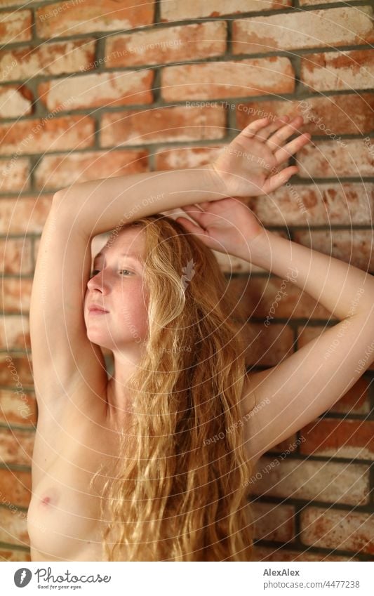 Portrait of a naked young woman with freckles and red hair pausing in a dancing pose in front of a brick wall portrait Near proximity Emanation tranquillity