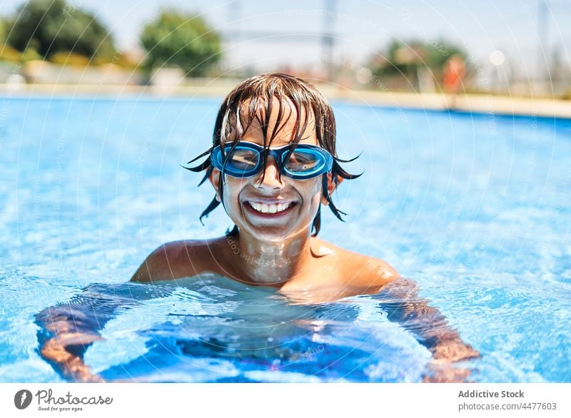 Cheerful boy in swimming goggles pool water happy smile summer kid wet hair child childhood glad joy weekend vacation daytime fun poolside sunlight pleasure