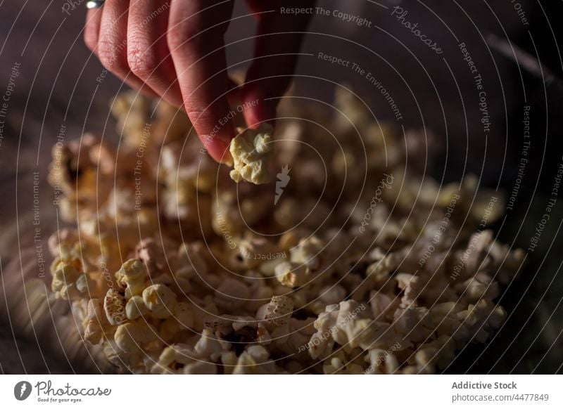 Anonymous woman sitting on sofa and eating popcorn couch legs crossed at home relax enjoy calm leisure apartment living room free time positive casual weekend