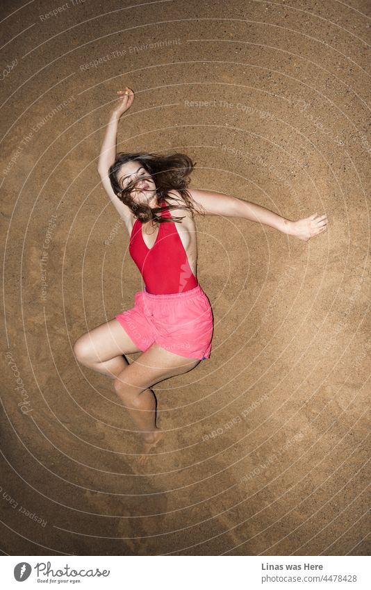 Gorgeous brunette model feeling cozy and relaxed on this hill of sand. Dressed in pink shorts and a red swimsuit, that can’t hide her sexy curves. The perfection of wild summer nights.