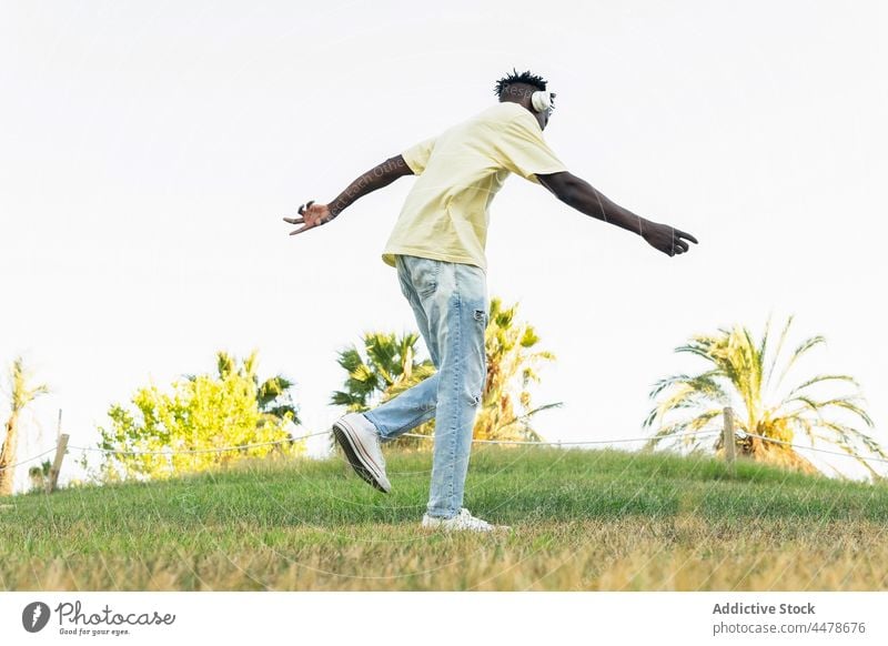 Anonymous black man in headphones standing among palms dance park casual music sun free time chill style rest listen sunlight calm palm tree freedom enjoy