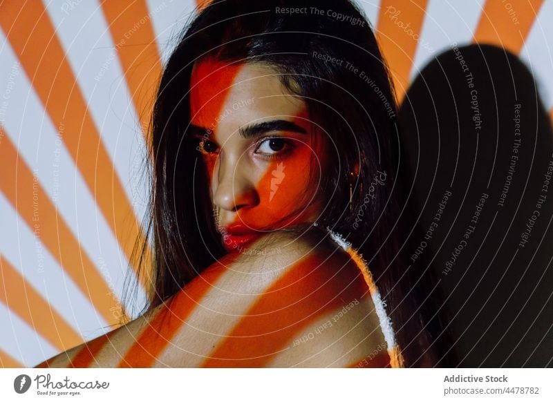 Trendy Hispanic model touching hair in projector light touch hair cool trendy individuality confident stare stripe woman portrait millennial contrast orange