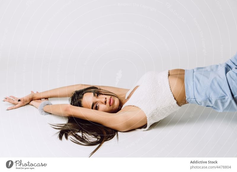 Stylish Hispanic model in crop top on light background fashion style individuality grace body cool appearance woman portrait trendy arms raised millennial gaze