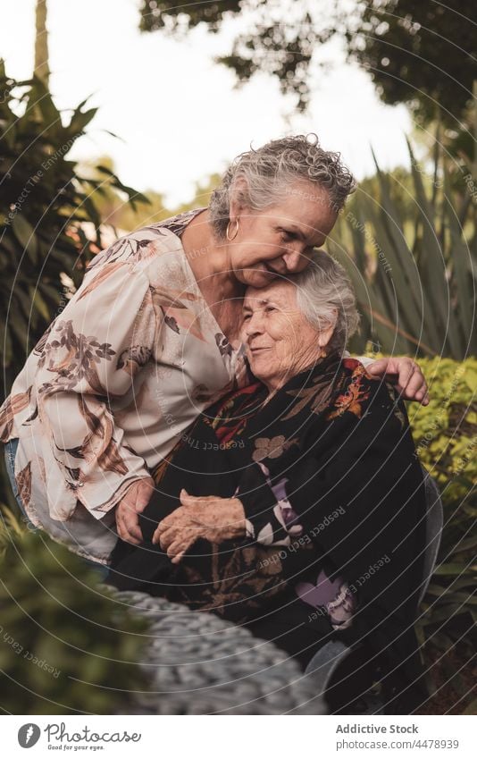 Senior woman kissing sister on head women garden happy hug love tender together weekend female elderly aged senior smile embrace park relationship cheerful joy