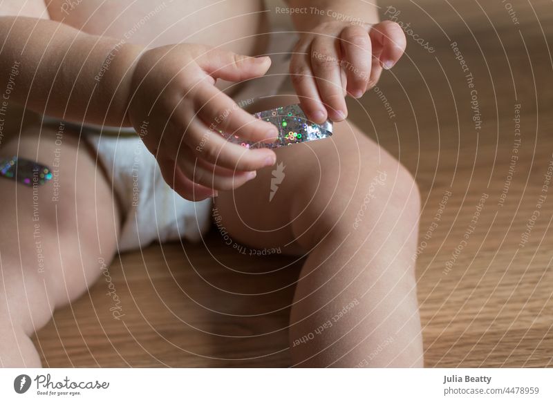 15 month old baby plays with a bandage after being given a vaccine in both legs vaccination vaccinate protect immune booster band-aid stick remove pull body