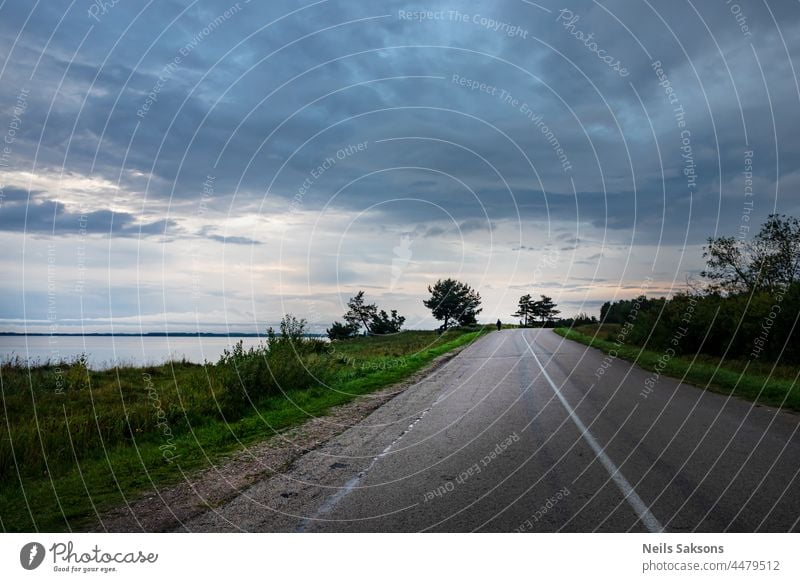 beautiful calm August evening near biggest Latvian lake Razna, asphalt road goes straihr near beach, cloudy sky, green grass on roadside open road solitude