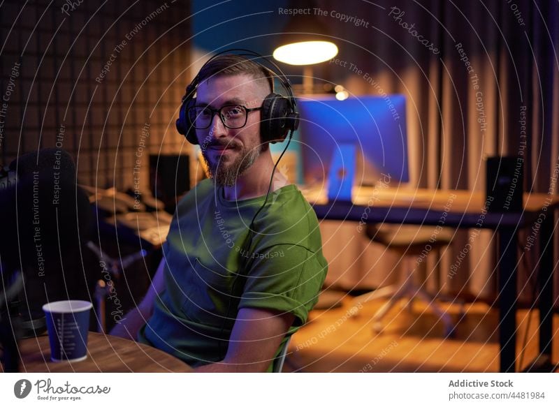 Male podcaster recording audio in studio man smile communicate positive radio entertain speak mic talk broadcast male young beard casual microphone eyeglasses