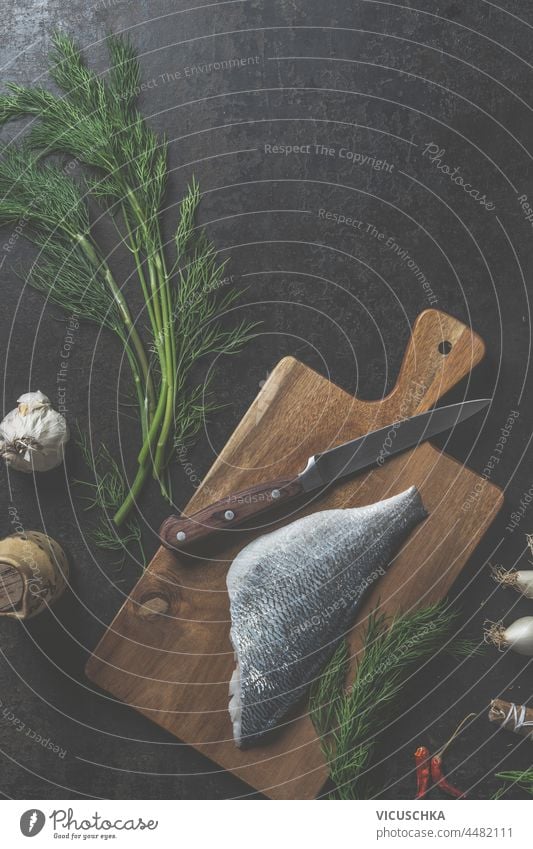 Dorado fish fillet on cutting board with knife , dill , north sea crab and other ingredients on dark kitchen table background. Top view dorado top view rustic