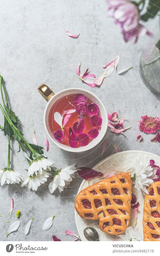 Heart shaped pastry with berries and pink flowers tea in white tea cup on white concrete kitchen table with flowers. Cozy, romantic tea time at home. Top view.