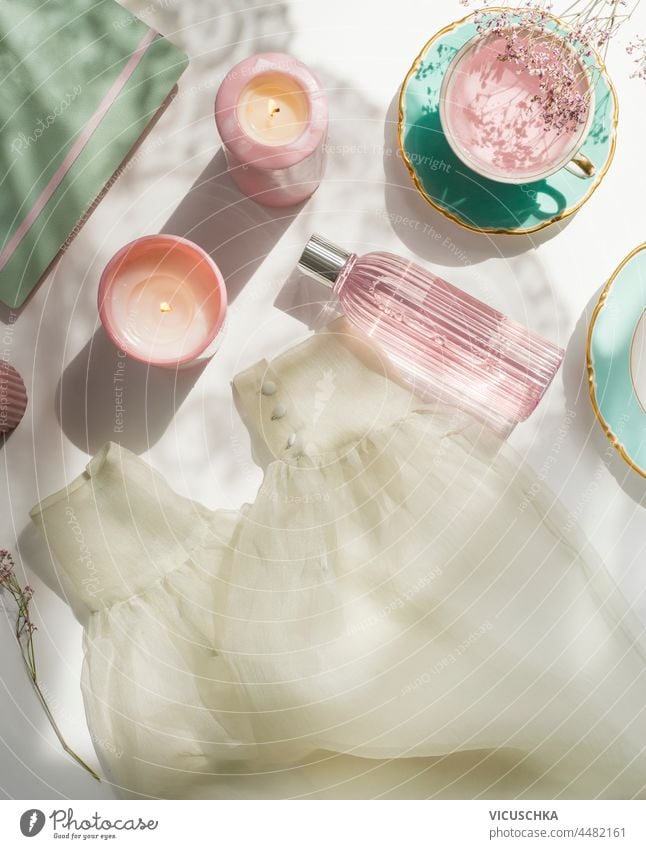 Women morning routine with tea, candles, facial toner in glass bottle, clothes, flowers and notepad on white background. Cozy morning at home with beauty products. Top view.