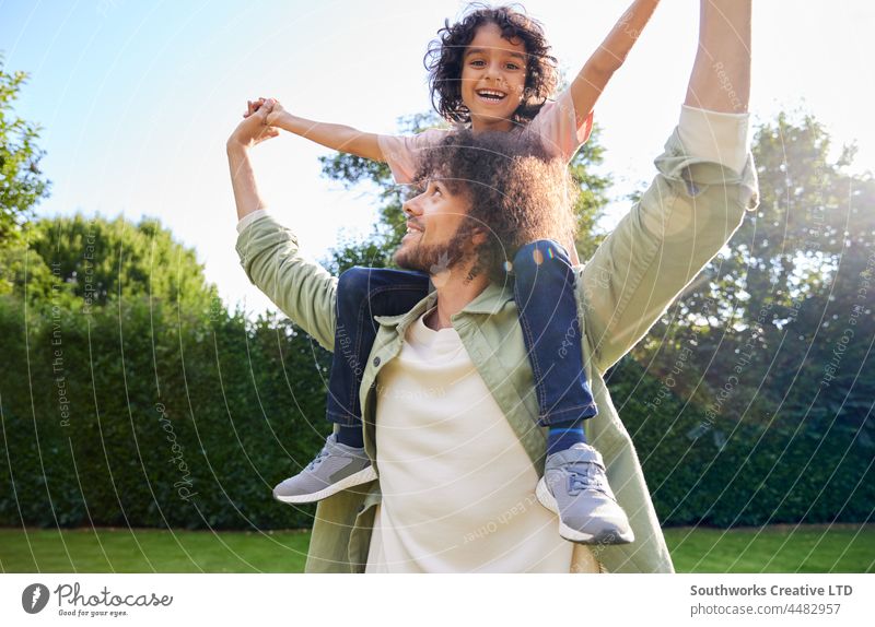 Father with son on shoulders and arm outstretched mixed race father carry smile boy child outdoors day two people portrait authentic childhood lifestyle happy