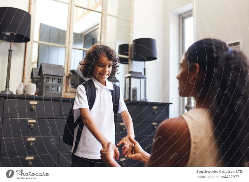 Mother holding son's hands before leaving for school uniform mixed race asian mother reassurance prepare support confidence indoors day home interior two people