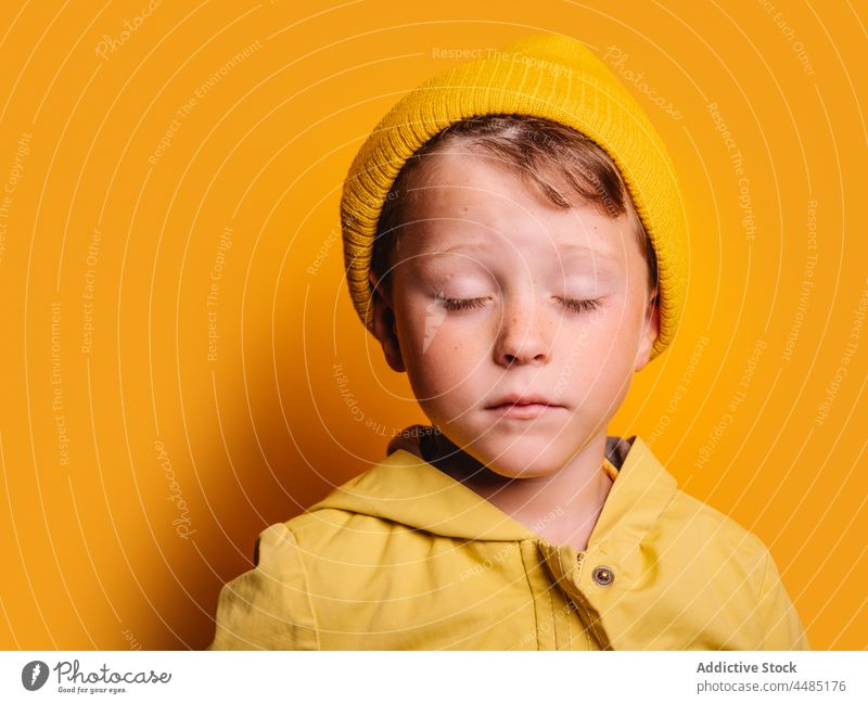 Calm boy in trendy outfit standing against yellow background calm childhood style individuality wear kid raincoat comfort zone pleasure little color cloth vivid