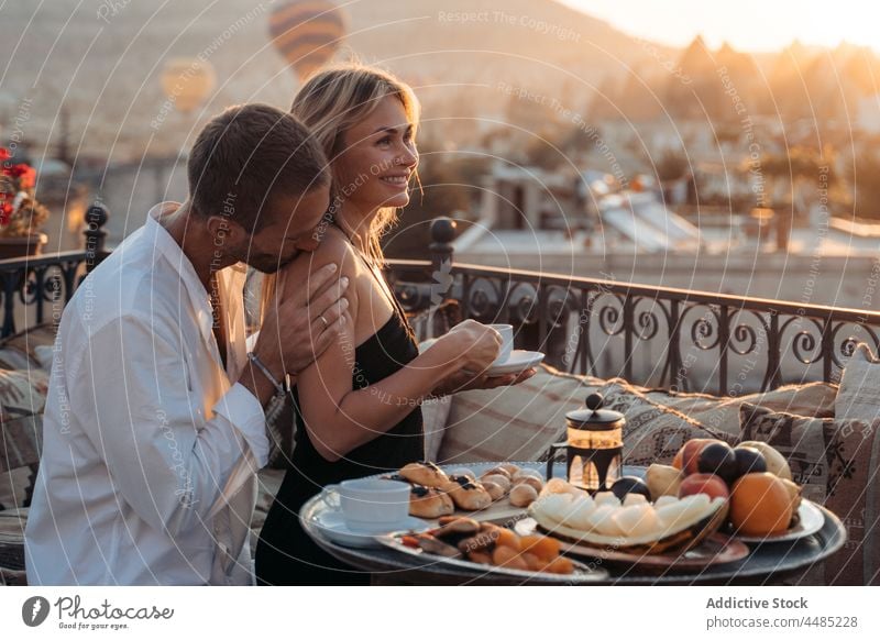 Guy kissing shoulder of wife on rooftop during date couple love terrace romantic dessert together bonding tea relationship enjoy tender affection delicious