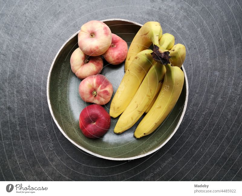 Round ceramic bowl with banana, peach and apple on grey concrete floor in a designer apartment do Rudersau near Rottenbuch in the district of Weilheim-Schongau in Upper Bavaria