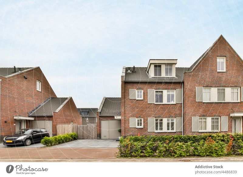 Brick houses on suburban street car bush summer architecture brick wall residential exterior building town facade cottage cloudy blue sky neighborhood dwell