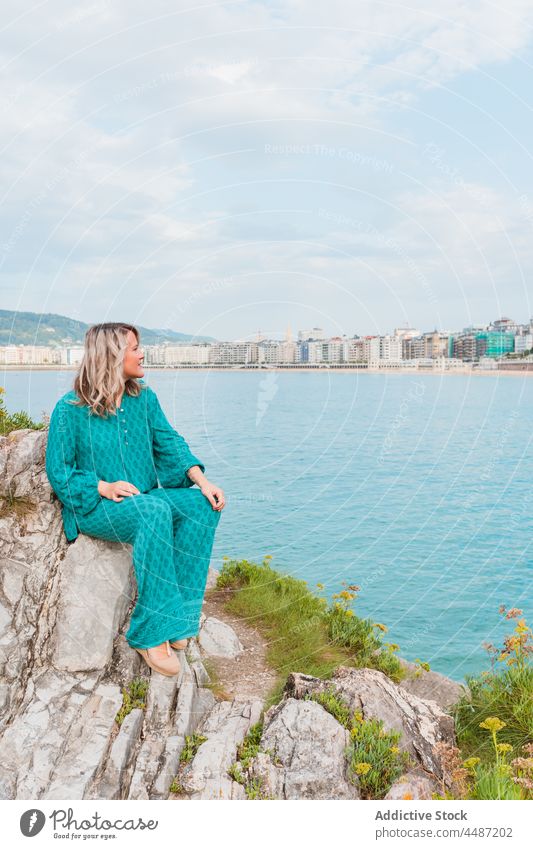 Dreamy woman sitting on rocks with green plants close to the sea style nature positive dreamy adjust environment female donostia trendy san sebastian charming