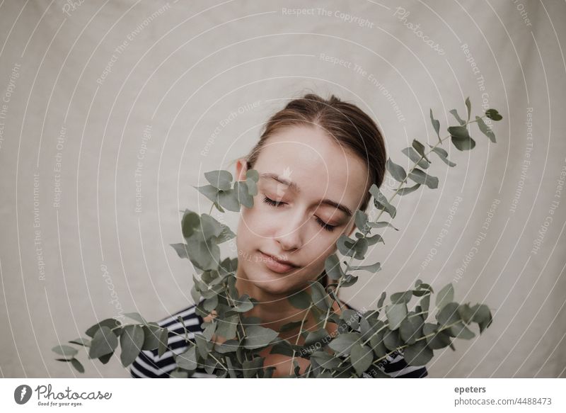 Young attractive woman with a eucalyptus branch and her eyes closed front of a linen canvas adult background beautiful beauty brunette caucasian delicate