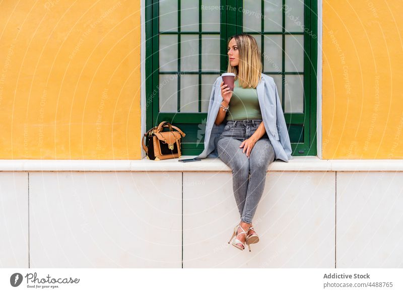 Stylish woman with takeaway coffee sitting near building drink street city beverage style caffeine trendy paper cup female to go cheerful positive glad optimist