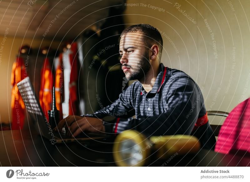 Thoughtful man using laptop at workplace computer station fireman firefighter browsing occupation busy professional concentrate male ethnic thoughtful focus