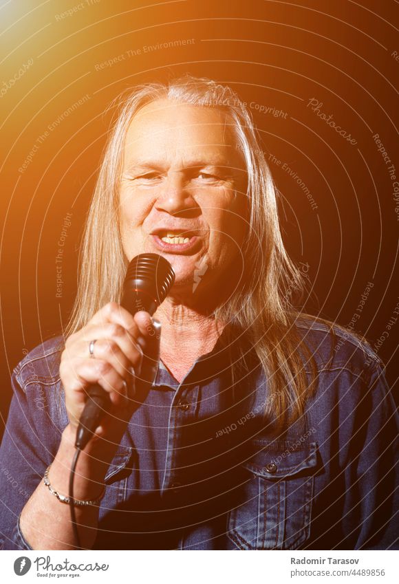 elderly man with long gray hair sings into a microphone long hair song stage black background music old senior male singer happy leisure fun mature concert