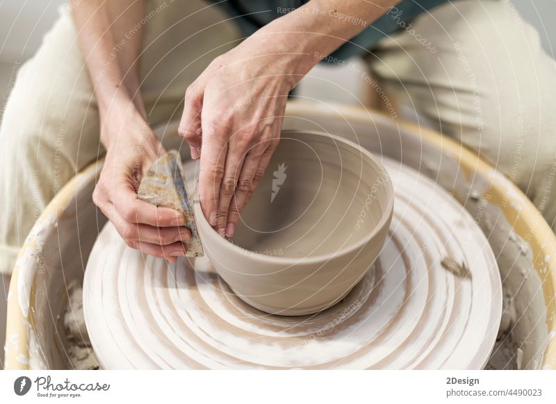 Hands of young woman working on pottery wheel in cozy workshop and making vase or mug clay hand closeup human hand ceramist artist creation skill wet hobby