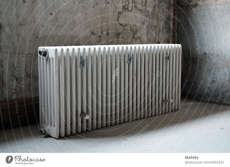 Old discarded radiator in the light in front of a grey balcony in a renovated farmhouse in Rudersau near Rottenbuch in the district of Weilheim-Schongau in Upper Bavaria