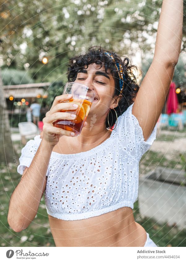 Carefree ethnic woman drinking cocktail during party dance summer enjoy celebrate glass garden female beverage smile cheerful weekend positive young refreshment