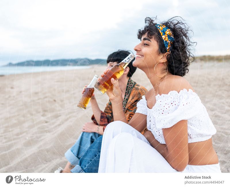 Happy diverse women drinking beer on beach laugh summer evening best friend alcohol together female multiethnic multiracial coast seashore weekend carefree