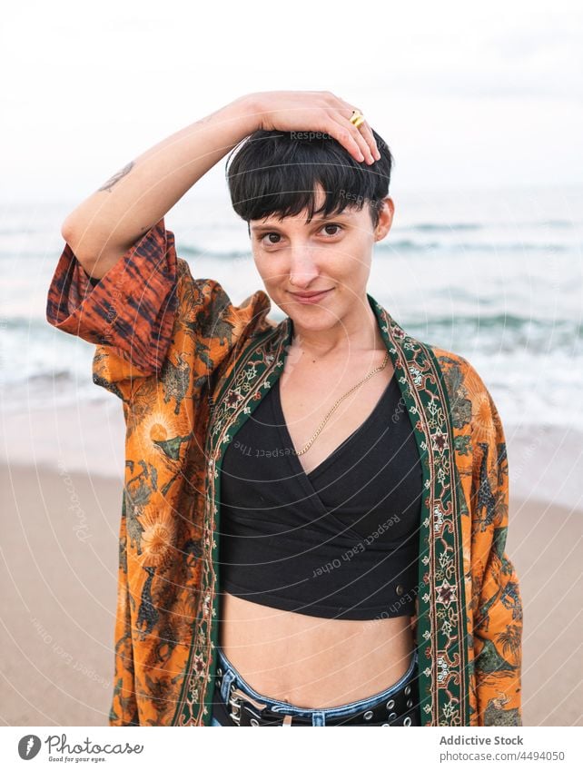 Woman standing on seashore in summer woman beach style smile trendy coast outfit touch head female happy cheerful individuality seaside glad optimist