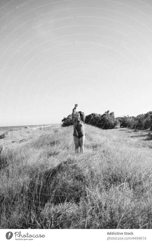 Unrecognizable woman standing on grassy meadow nature summer sky cloudless countryside environment peaceful female field flora alone shirt calm daytime bush