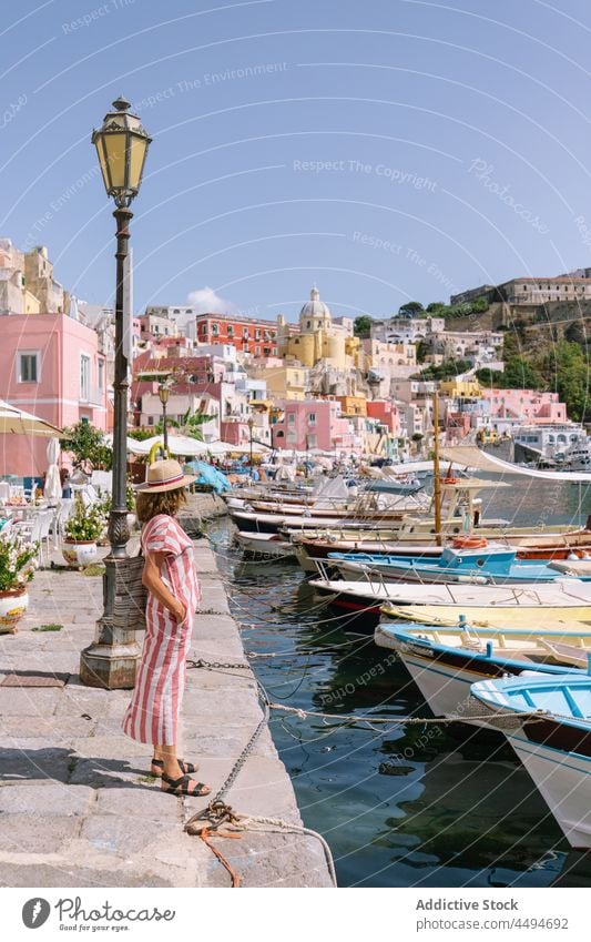 Woman standing on embankment near sea in coastal town woman boat moor style port shore female procida italy flegrean islands hat dress calm waterfront alone