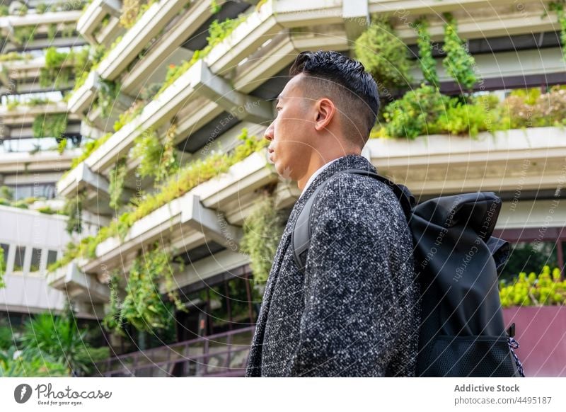 Stylish Asian businessman with backpack against contemporary buildings in city entrepreneur well dressed rucksack contemplate haircut modern natural style