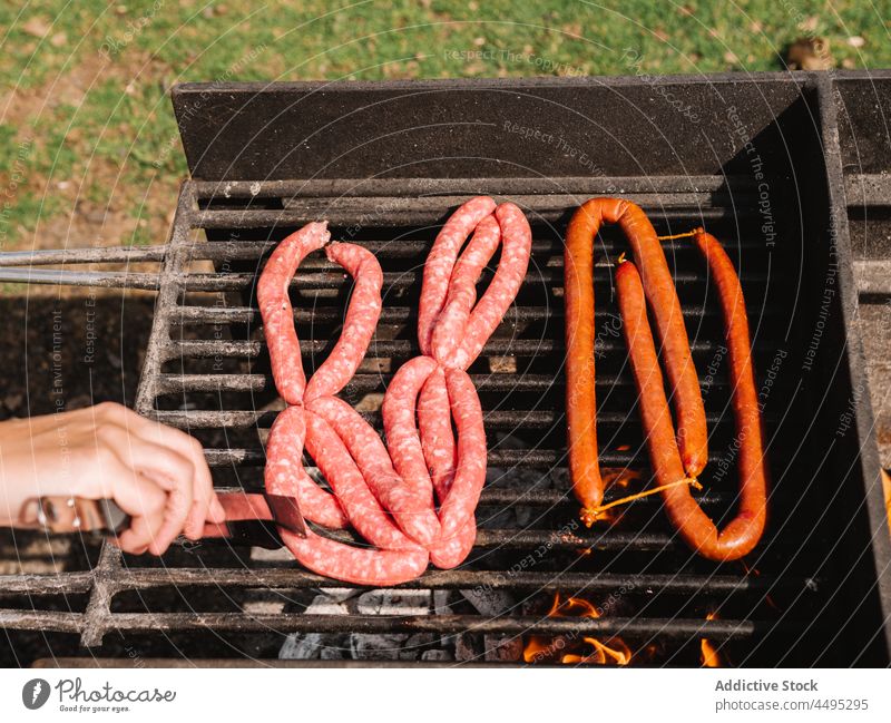 Anonymous person frying sausages on grill in countryside meat barbecue roast charcoal grate bbq food tasty summer delicious picnic yummy fresh hot various