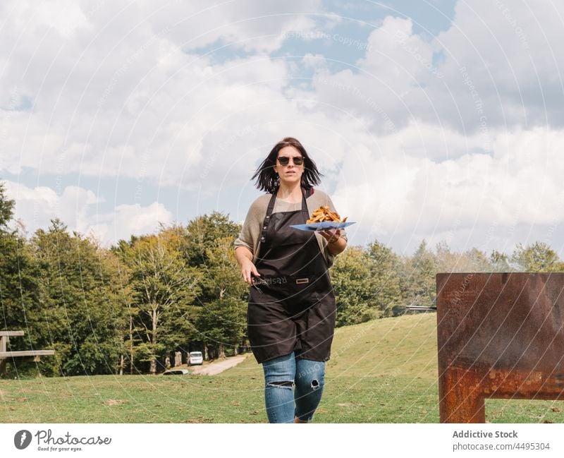 Woman with grilled chicken walking on lawn woman cook wing meat roast countryside rural barbecue field bbq food tasty summer plate carry chef delicious picnic