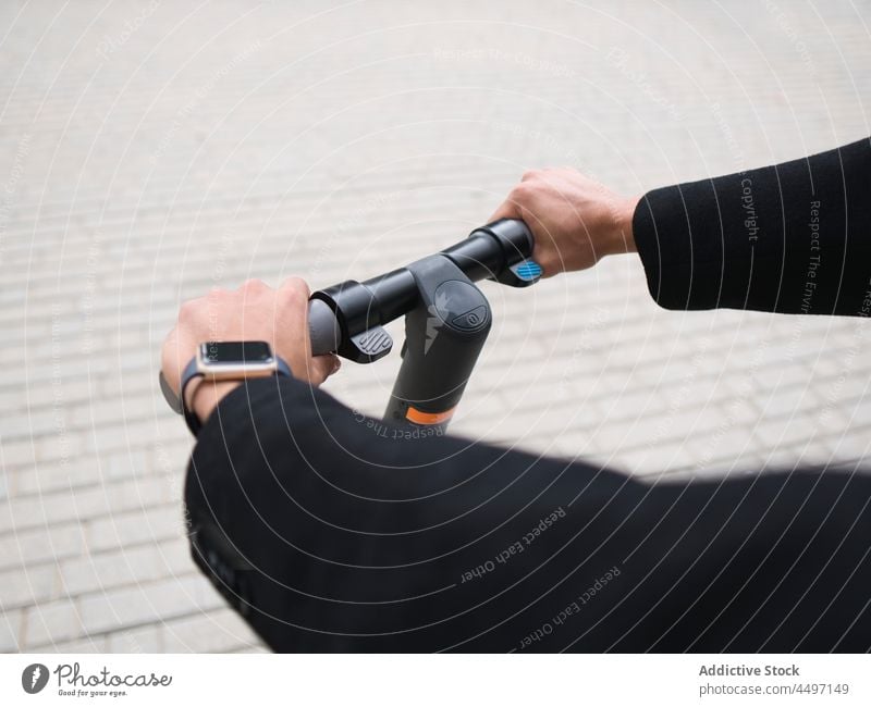 Crop stylish man riding e scooter on street ride trendy electric transport city vehicle style pavement modern male young active smart watch move cool