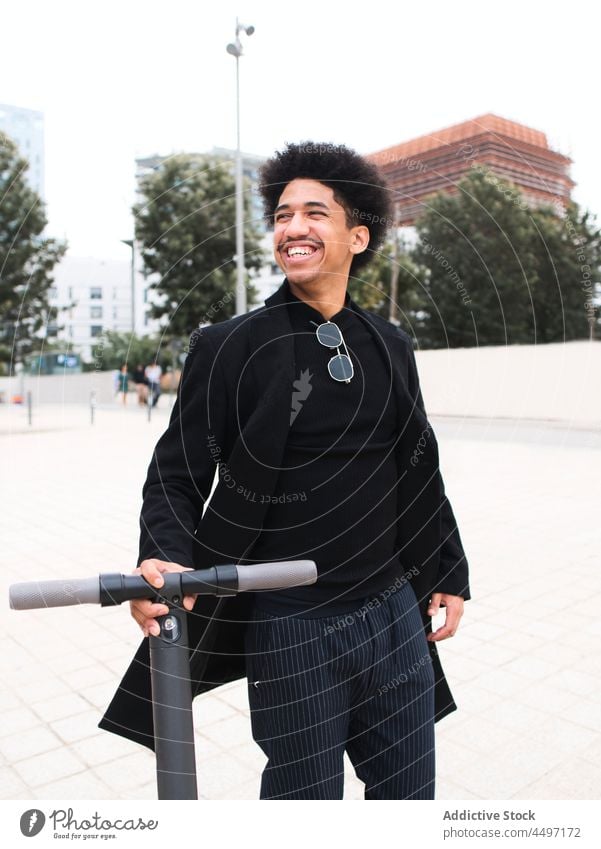 Confident stylish ethnic man with scooter standing on city square walk self assured trendy street ride style fashion confident smile positive millennial male