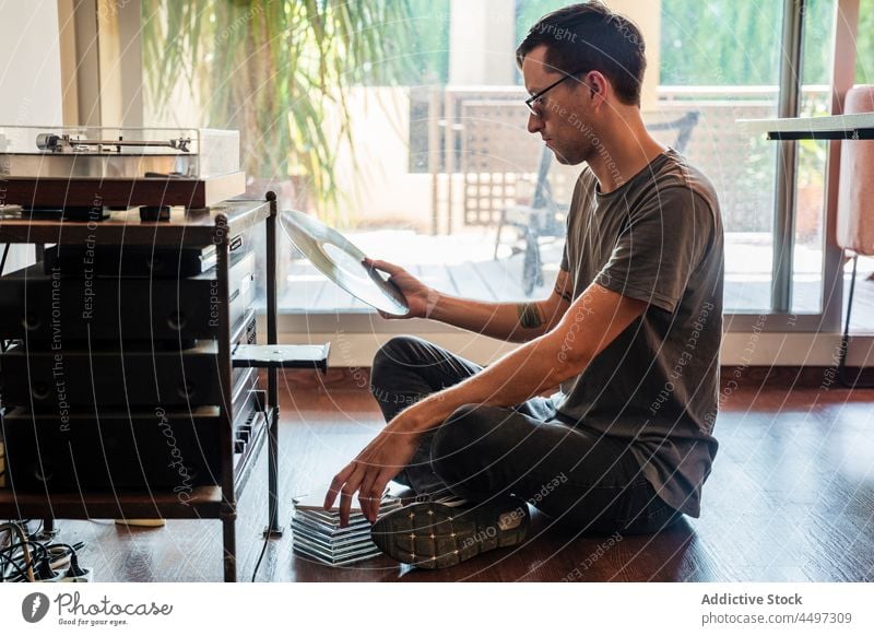 Guy looking at vinyl record while sitting near player man turntable floor music concentrate nostalgia vintage retro male old fashioned lifestyle focus