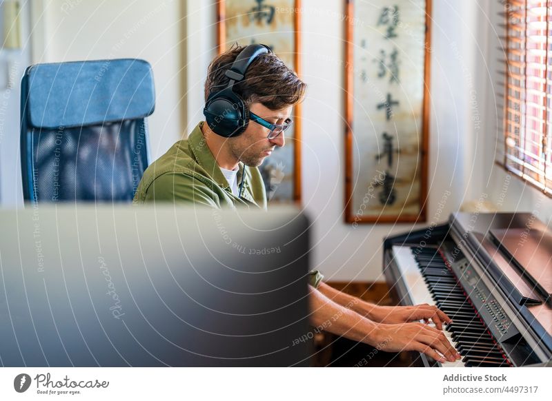 Male musician playing on piano in light room man pianist headphones compose instrument melody practice talent male window sit casual hobby keyboard skill