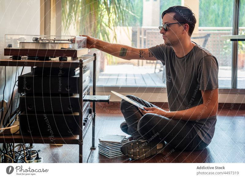 Guy looking at vinyl record while sitting near player man turntable floor music concentrate nostalgia vintage retro male old fashioned lifestyle focus