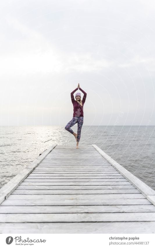 Woman in sportswear doing yoga on jetty in front of sea Yoga Footbridge Autumn Sportswear Ocean Lake Fitness bank Healthy workout Athletic Wellness Lifestyle