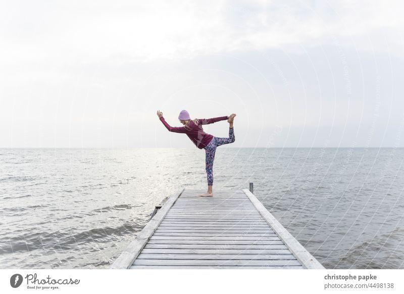 Woman in sportswear doing yoga on jetty in front of sea Yoga Footbridge Autumn Sportswear Ocean Lake Fitness bank Healthy workout Athletic Wellness Lifestyle