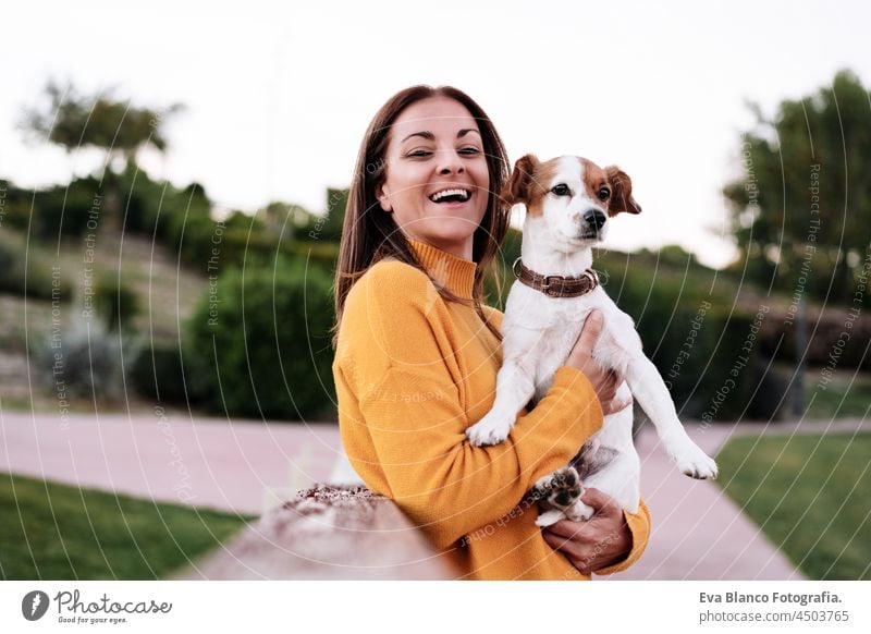 happy caucasian woman having fun with jack russell dog in park,woman holding pet during autumn season. Pets and love concept kiss enjoy lick together