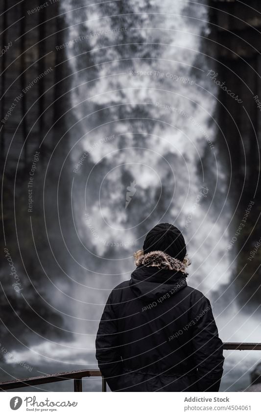 Unrecognizable traveler recreating while admiring powerful rapid waterfall on cloudy day person admire nature trip scenic stream vacation breathtaking explore