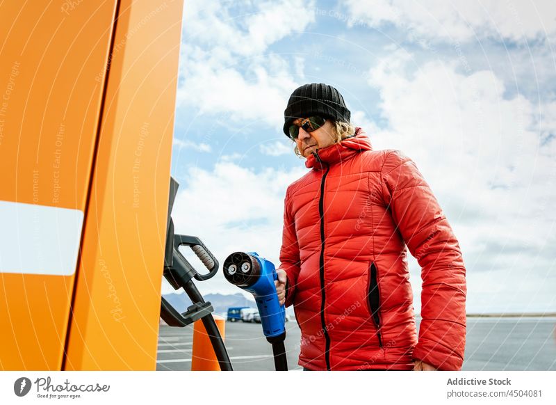 Man standing with charging power to electric vehicle at gas station man pensive thoughtful charge car ecology male transport sunglasses energy auto modern