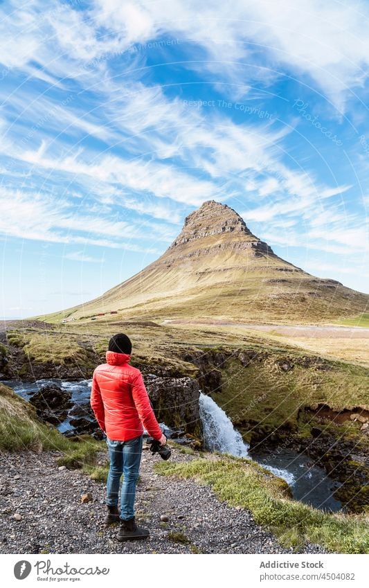 Traveler standing near waterfall and admiring picturesque landscape of mountain man photographer admire spectacular photo camera scenery outerwear nature male