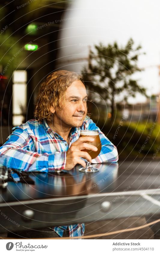 Pensive man drinking beer in bar in daylight alcohol thoughtful beverage pensive pub sit male casual glass calm curly hair restaurant serious daytime guy alone